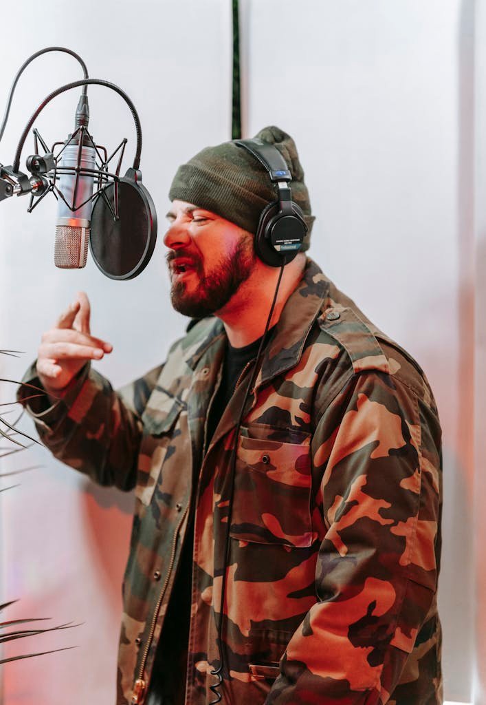 Musician Lyrics in studio wearing headphones and camo jacket, mid-song expression.