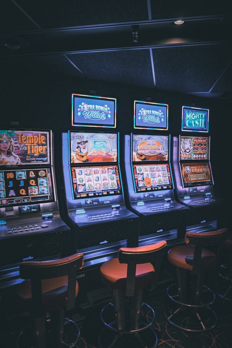 Row of illuminated 777 Slots machines in a dimly lit, empty casino area.thisvidscat.org