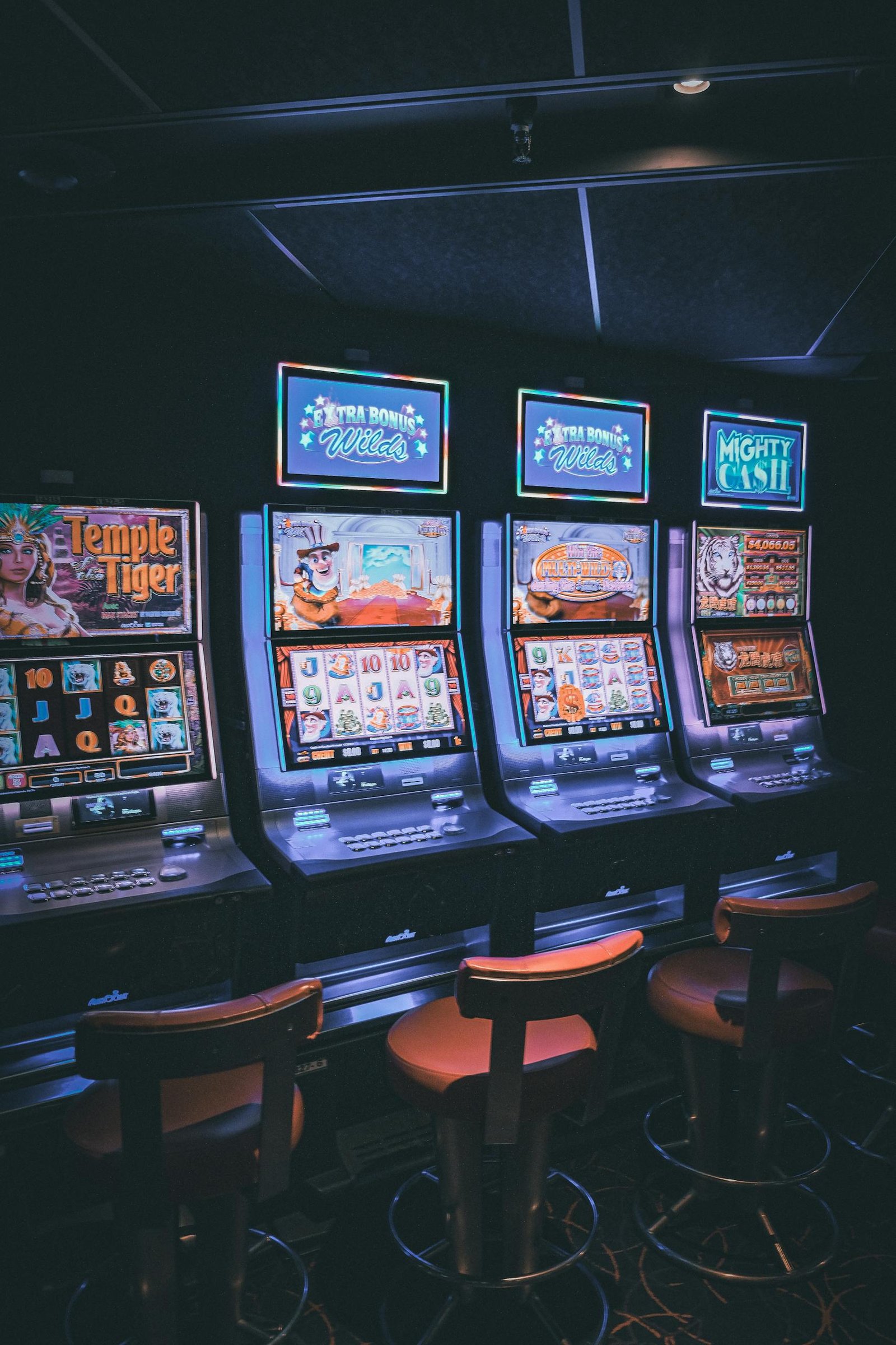 Row of illuminated 777 Slots machines in a dimly lit, empty casino area.thisvidscat.org