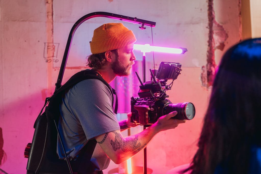 Cameraman operating camera on film set with colorful lighting in creative environment.