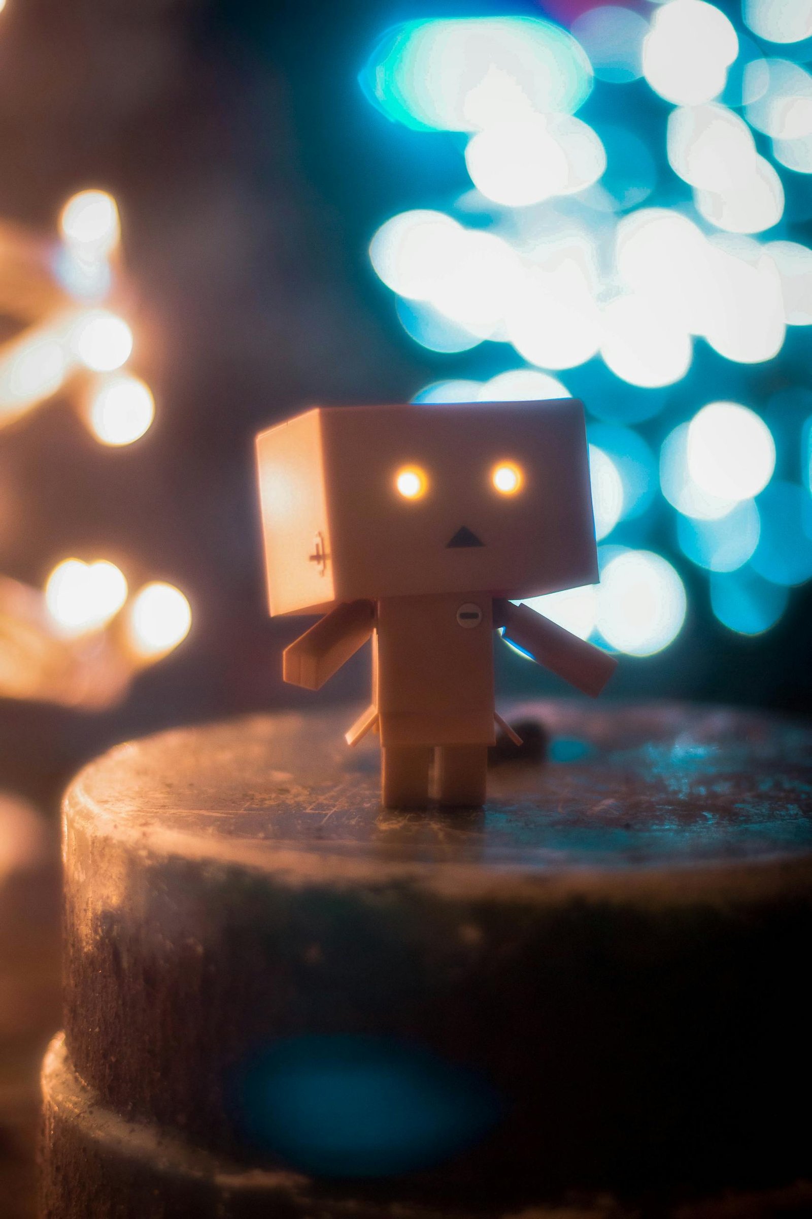 Cardboard ThisVideoBot toy with glowing eyes against a bokeh light background, creating a magical atmosphere.thisvidscat.org