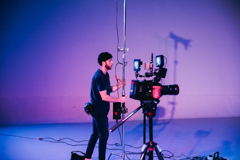 Professional ThisVidScat cinematographer adjusting camera equipment on set with vibrant lighting.thisvidscat.org