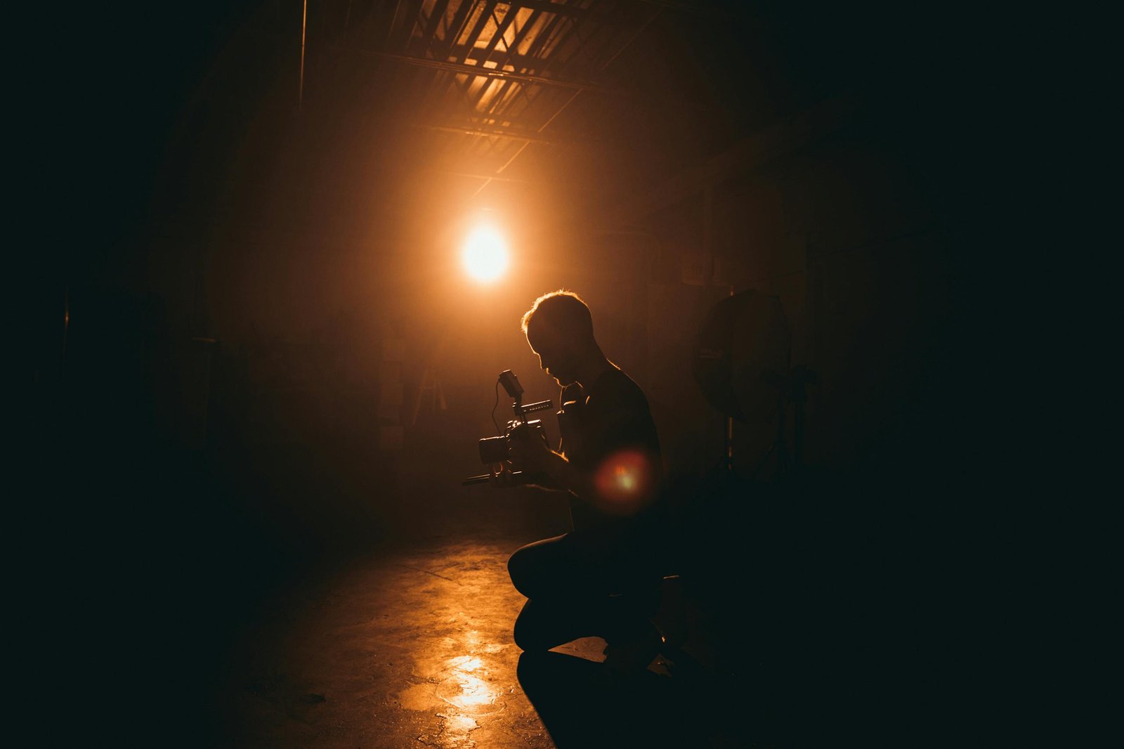 Silhouette of a This Vid Vore cinematographer operating a camera in a dimly lit studio with dramatic lighting.
